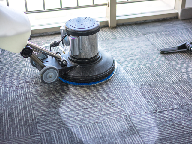 Rotary floor buffer with bonnet pad resting on commercial carpet tiles